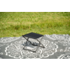 Petit tabouret pliant noir sur une couverture grise à motif floral blanc sur de l'herbe verte