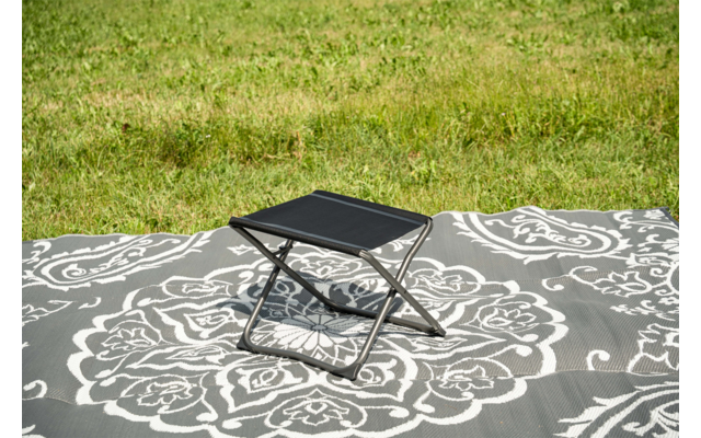 Petit tabouret pliant noir sur une couverture grise à motif floral blanc sur de l'herbe verte