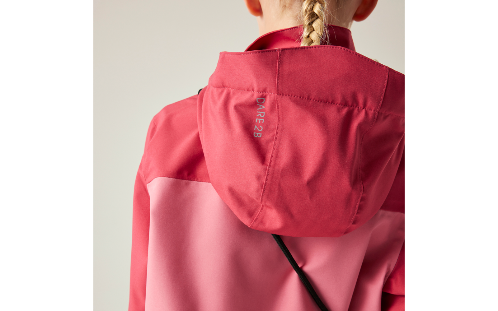 Person von hinten, blond geflochtener Zopf, trägt eine pink-rote Kapuzenjacke mit der Beschriftung "DARE2B" auf der Kapuze und einem diagonalen schwarzen Riemen über dem Rücken