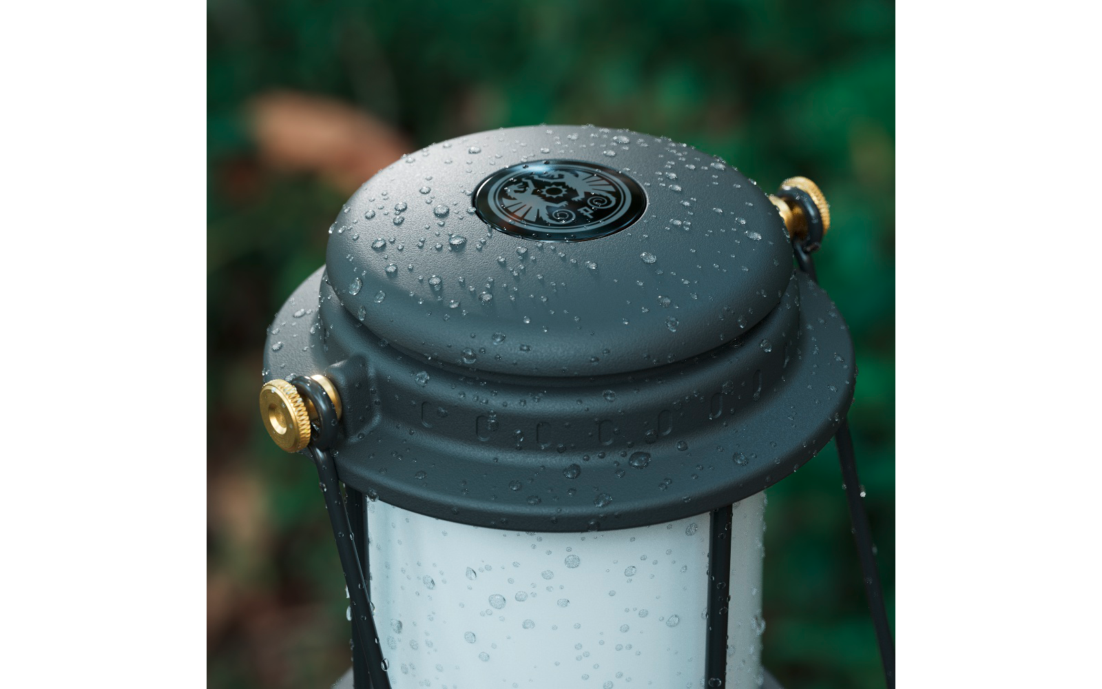 Primo piano della parte superiore metallica bagnata di una lanterna con gocce d'acqua, viti dorate e vetro bianco lattiginoso su sfondo verde sfocato