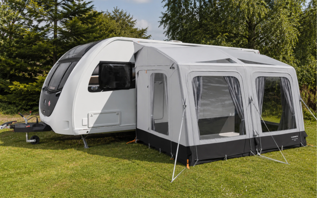 White caravan with a gray awning attached, on grass with trees in the background