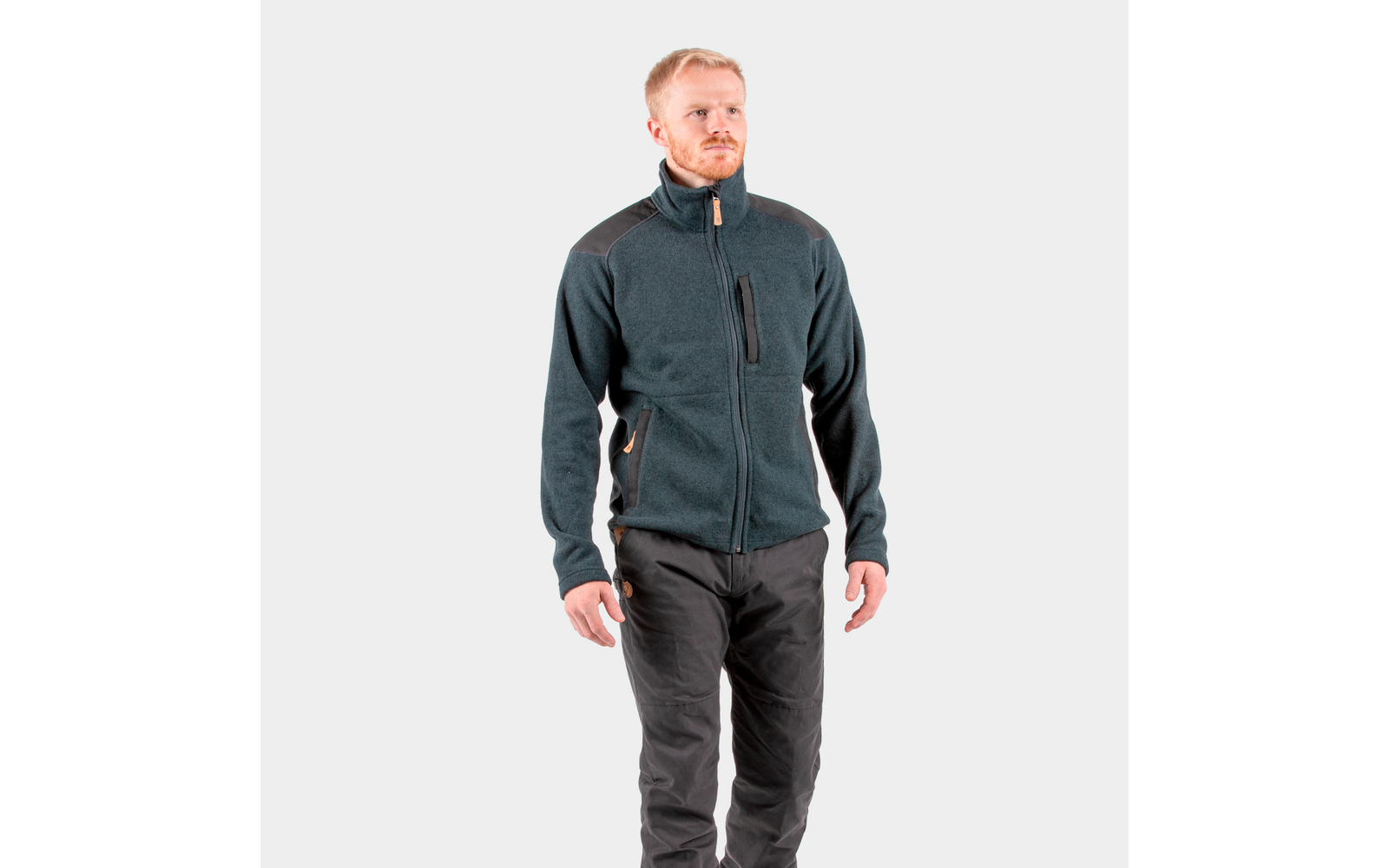 Een man draagt een donkergrijs jack en zwarte broek, staat en kijkt naar rechts