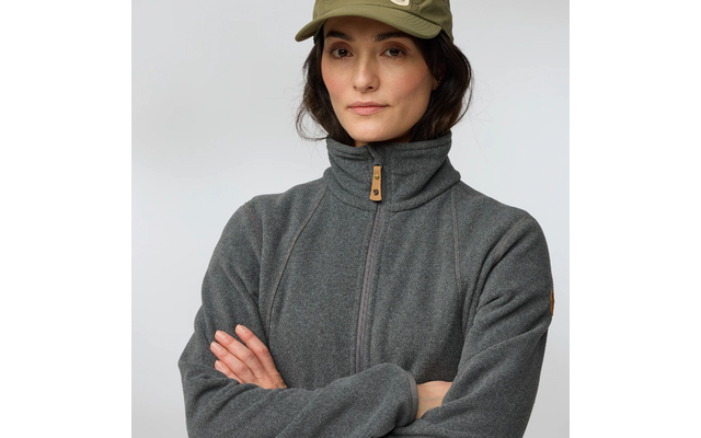 Personne en buste, porte une polaire grise à fermeture éclair et col montant, casquette baseball vert olive, bras croisés, fond uni clair