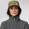Personne portant une casquette vert olive avec logo, cheveux foncés et veste polaire grise sur fond neutre