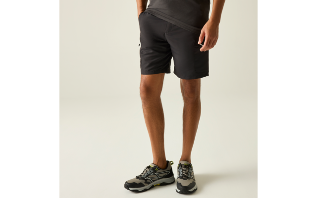 Bas du corps d'une personne portant un short noir et des baskets gris et noirs avec des accents verts sur un fond clair