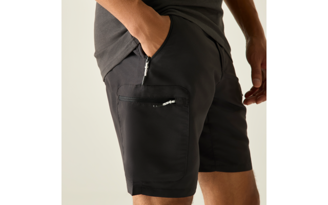 Hanches et cuisses d'une personne portant un short noir avec une poche latérale zippée, une main dans la poche avant