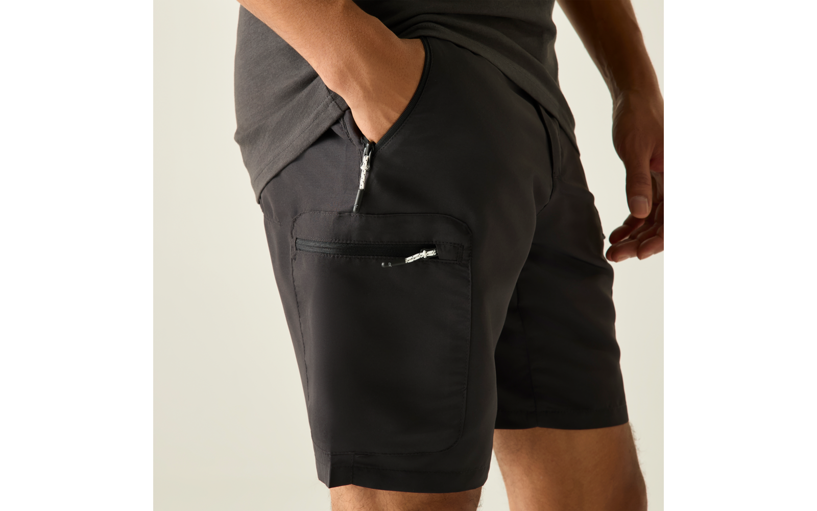 Hanches et cuisses d'une personne portant un short noir avec une poche latérale zippée, une main dans la poche avant