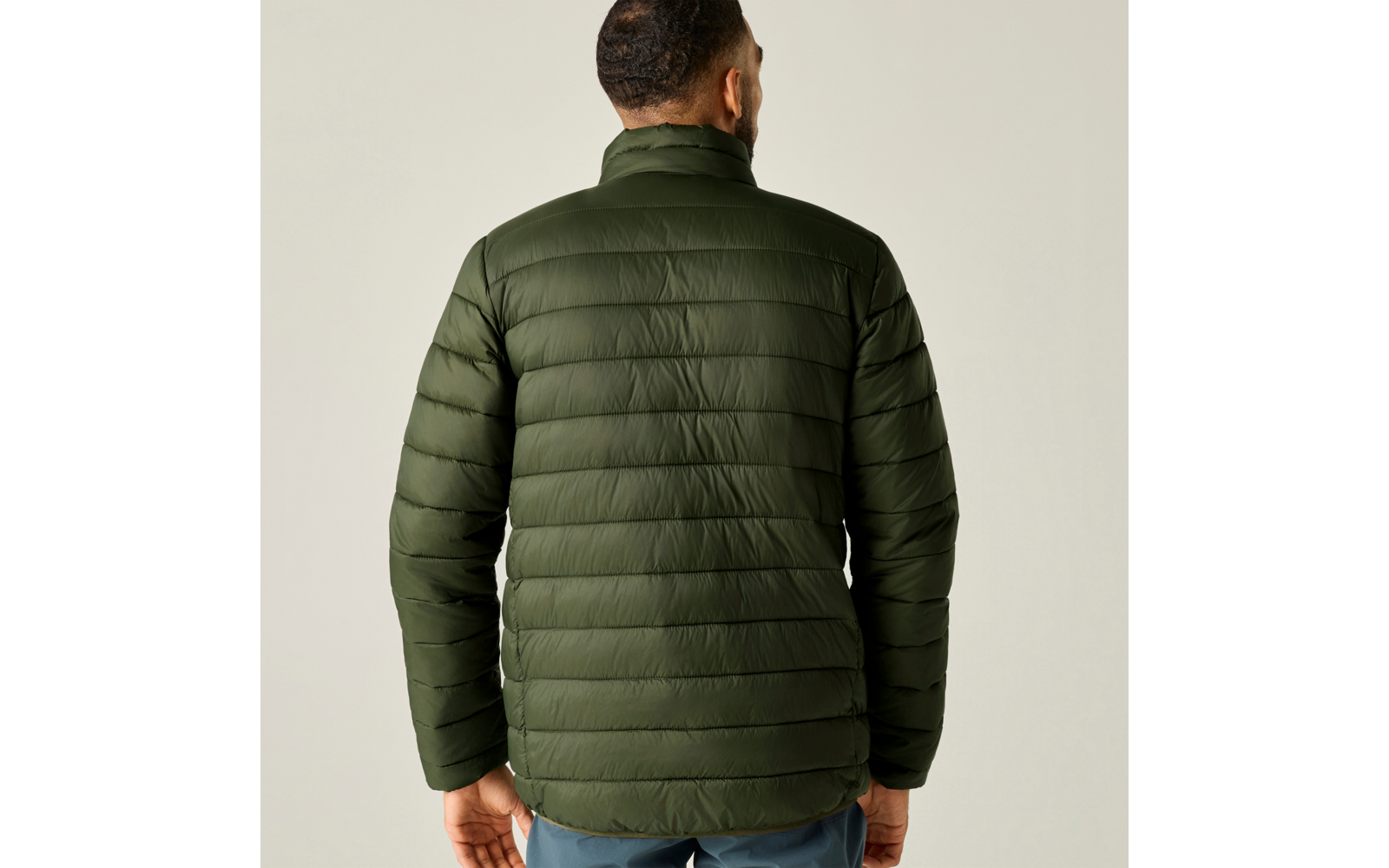 Achteraanzicht van een persoon met een olijfgroene doorgestikte jas en een blauwe broek voor een lichte achtergrond