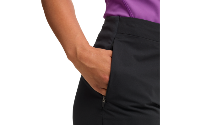 Nahaufnahme einer Hand in der seitlichen Reißverschlusstasche einer schwarzen Hose; violettes Oberteil sichtbar