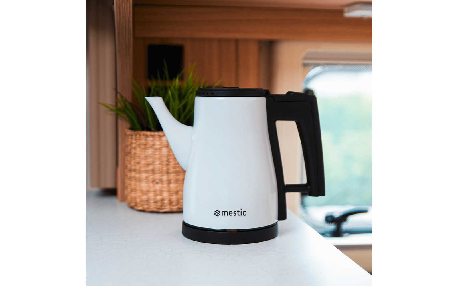 White electric kettle on a white countertop, with a woven basket and plant in the background