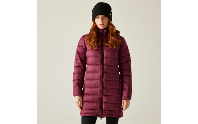 Femme aux longs cheveux roux portant une veste matelassée violette-grise et un bonnet noir, debout devant un fond blanc