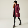 Femme portant un bonnet foncé, un long manteau bordeaux, un pantalon noir et des baskets marchant vers la droite sur fond clair