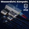 Metallisches rechteckiges Elektronikmodul mit drei Kühlkörpern, angeschlossenen schwarzen Kabeln mit roten und blauen Litzen, Wassertröpfchen auf dem Modul, dunkelblauer strukturierter Hintergrund. Oben weißer Text 'Wasserdicht. Kompakt.' und rechts 