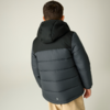 Person von hinten, trägt dunkle gesteppte Kapuzenjacke und hellbeige Hose, neutraler heller Hintergrund