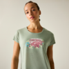 Frau vor hellem Hintergrund, trägt hellgrünes T-Shirt mit rosa Campervan-Illustration und Blumen