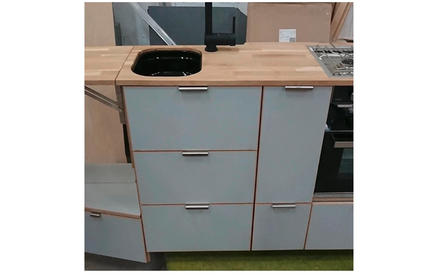 Keukenblok met houten werkblad, zwarte spoelbak en kraan, lichtblauwe kastfronten met metalen handgrepen, linker lade open, rechts fornuis en oven zichtbaar