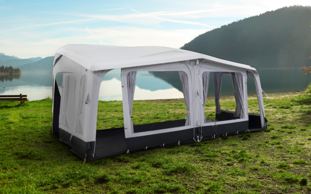 Großes, weißes und graues Gartenzelt mit gewölbtem Dach auf einer Wiese vor einem See und Bergen im Hintergrund