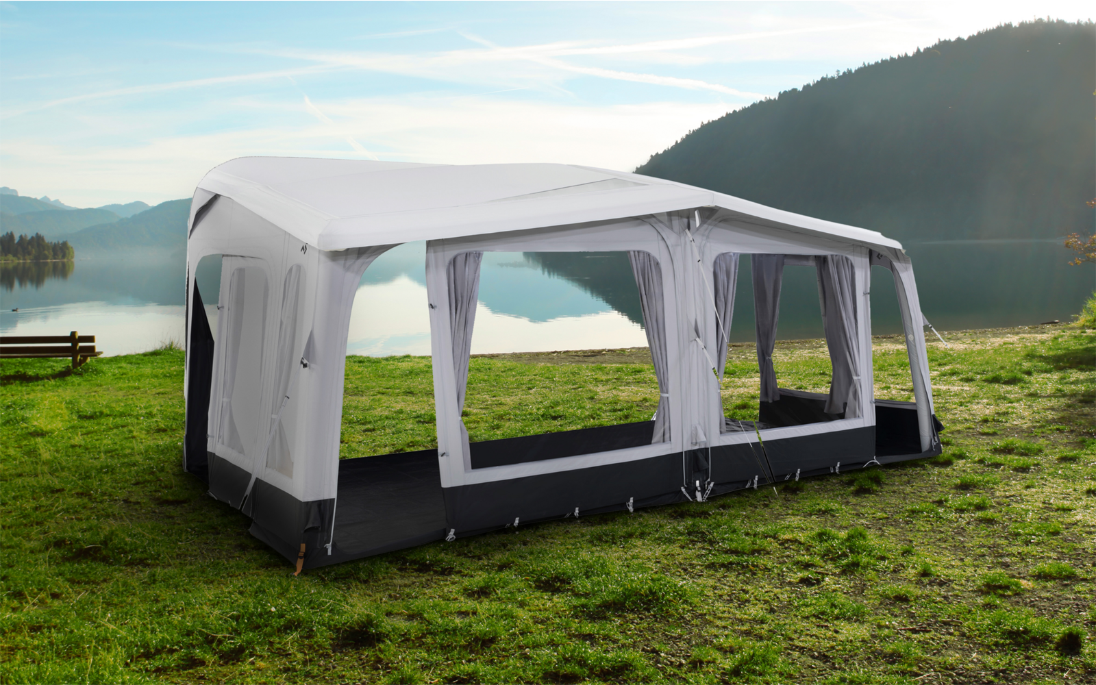 Großes, weißes und graues Gartenzelt mit gewölbtem Dach auf einer Wiese vor einem See und Bergen im Hintergrund