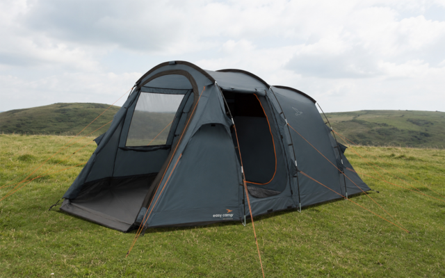 Donkergrijs tunneltent met open ingang en muskietennet, oranje scheerlijnen, op een grasheuvel onder een bewolkte lucht