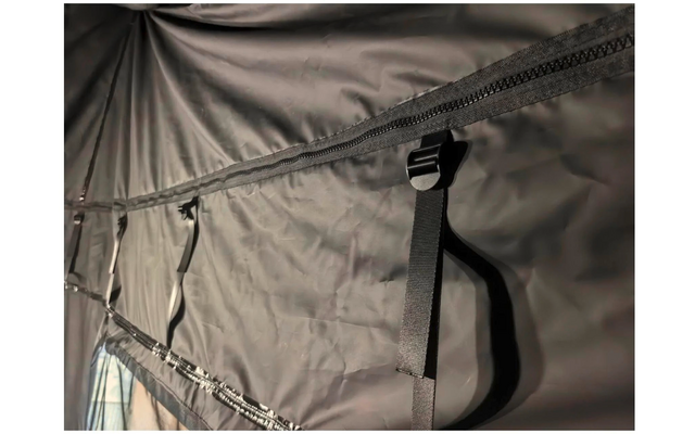 tissu synthétique foncé avec une fermeture éclair horizontale, une sangle noire avec boucle en plastique pendante, coutures et plis visibles, ouverture en tissu clair avec fermeture éclair en bas à gauche