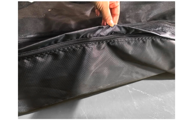 Main tenant une poche zippée ouverte en tissu noir texturé ; surface grise visible en dessous
