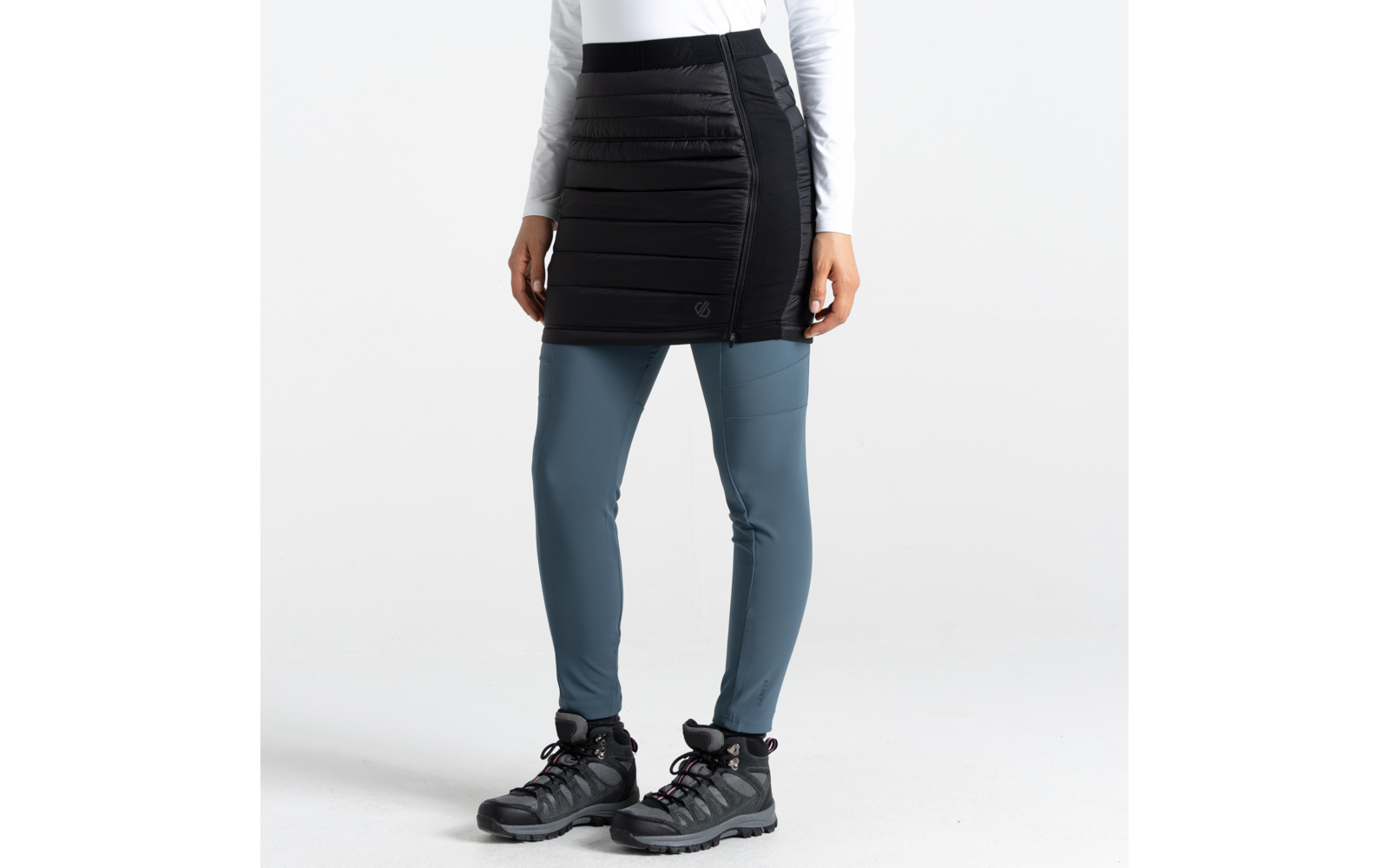 Partie inférieure du corps d'une femme portant un pantalon jupe noir, des leggings bleus et des chaussures noires sur fond blanc