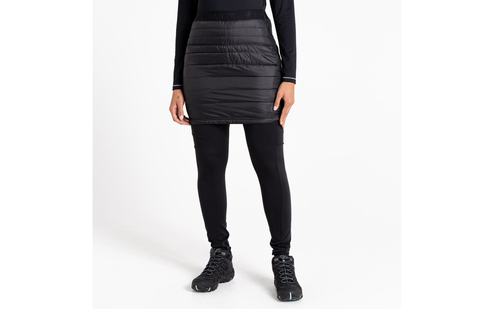 Femme portant une jupe noire, des leggings noirs et des chaussures noires, debout sur fond blanc