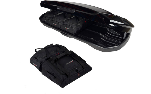 Coffre de toit noir ouvert contenant plusieurs sacs de voyage noirs, un grand sac de voyage posé à côté sur fond blanc