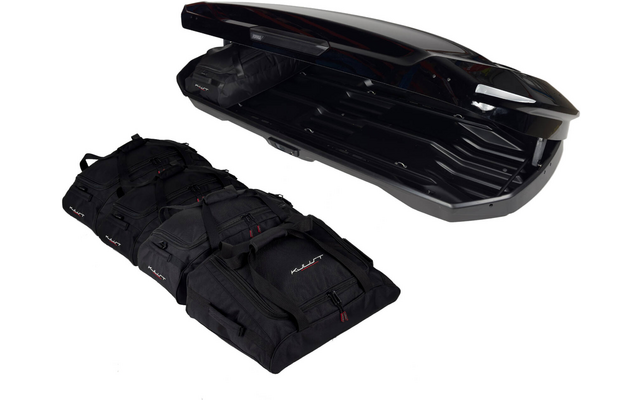 Coffre de toit noir ouvert avec intérieur visible à côté de trois sacs de voyage noirs sur fond blanc