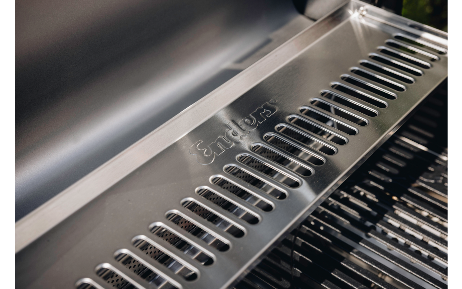 Nahaufnahme eines Edelstahlgehäuses mit gelochter Metallplatte, eingraviertem Schriftzug "Enders" und sichtbaren Grillrosten