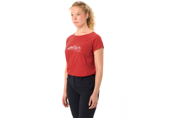 Person mit blonden, lockigen Haaren zu einem Pferdeschwanz gebunden, trägt ein rotes T-Shirt mit weißem Logo, blickt nach links vor weißem Hintergrund