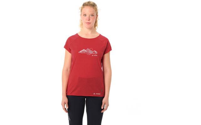 Person steht frontal vor weißem Hintergrund, trägt rotes kurzärmeliges T-Shirt mit Berggrafik und schwarze Hosen, blonde zusammengebundene Haare, Arme seitlich entspannt