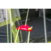 Red plastic rope tensioner piece with two yellow tent cords threaded through; tent fabric and metal poles visible in the background