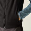 Bovenlichaam van een persoon met een zwart fleecevest over een blauw gemêleerd shirt met lange mouwen, rechterhand in de zak van het vest