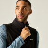 Persoon trekt aan de rits van een zwart fleecevest, draagt een blauw shirt met lange mouwen, kijkt naar links, lichte achtergrond