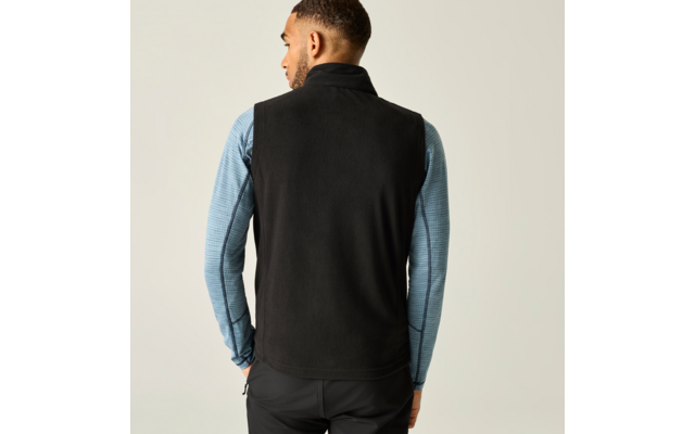 Persoon van achteren, draagt zwart mouwloos fleecegilet over lichtblauw shirt met lange mouwen, voor een lichte achtergrond