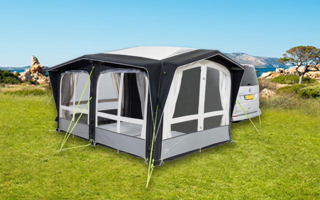 Wohnwagen mit angebautem grauem Vorzelt auf einer grünen Wiese bei klarem Himmel