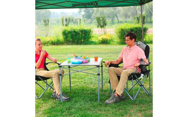 Deux personnes assises sur des chaises de camping en plein air, avec une petite table pliante et des tasses colorées entre elles