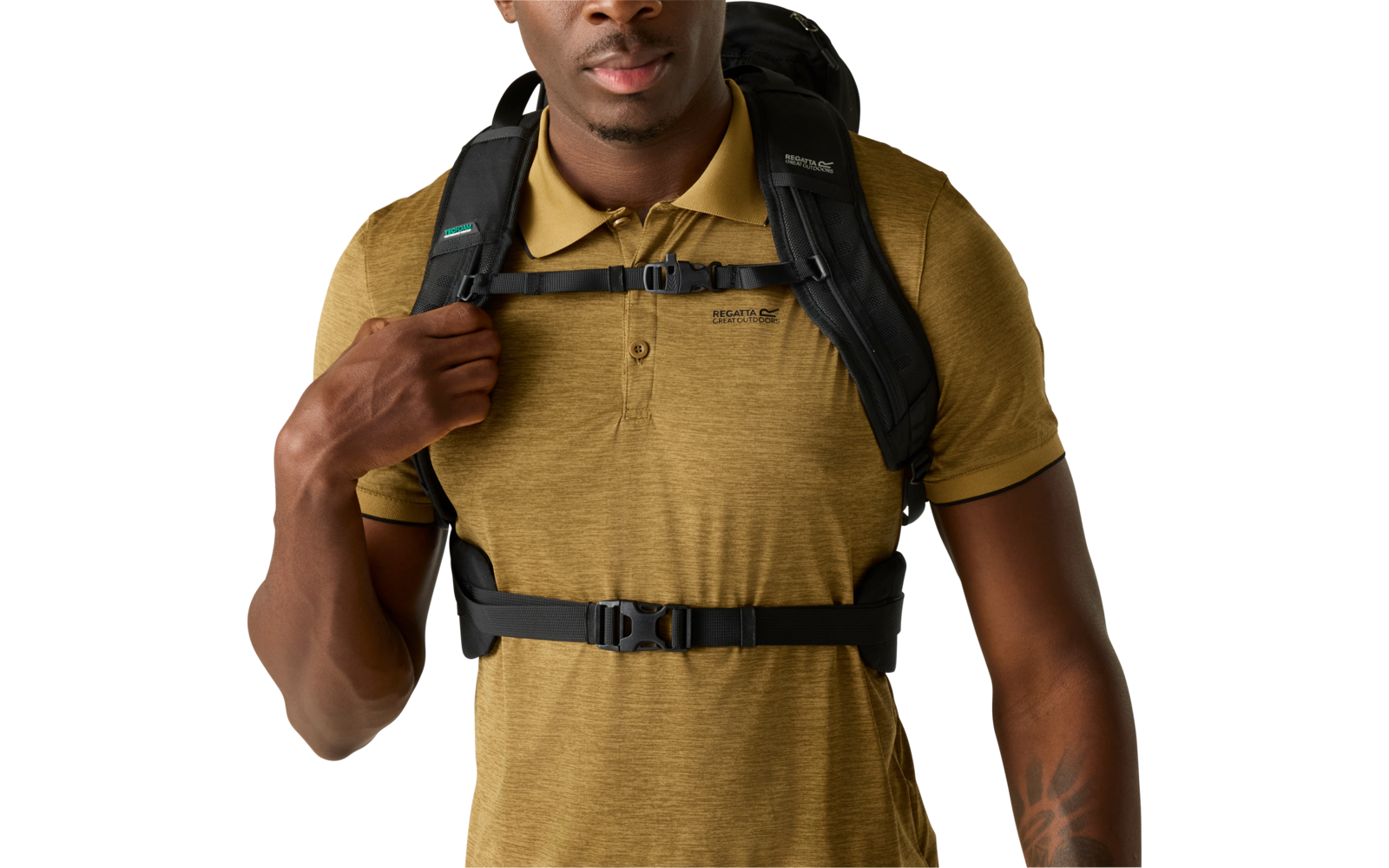 Oberkörper einer Person mit senfgelbem Polohemd und schwarzem Rucksack mit Brust- und Hüftgurt; eine Hand hält den Schultergurt; Unterarm mit Tattoo sichtbar