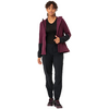 Femme aux cheveux courts et foncés portant un pull rouge foncé, une veste noire, un pantalon noir et des chaussures noires, tenant un sac rouge