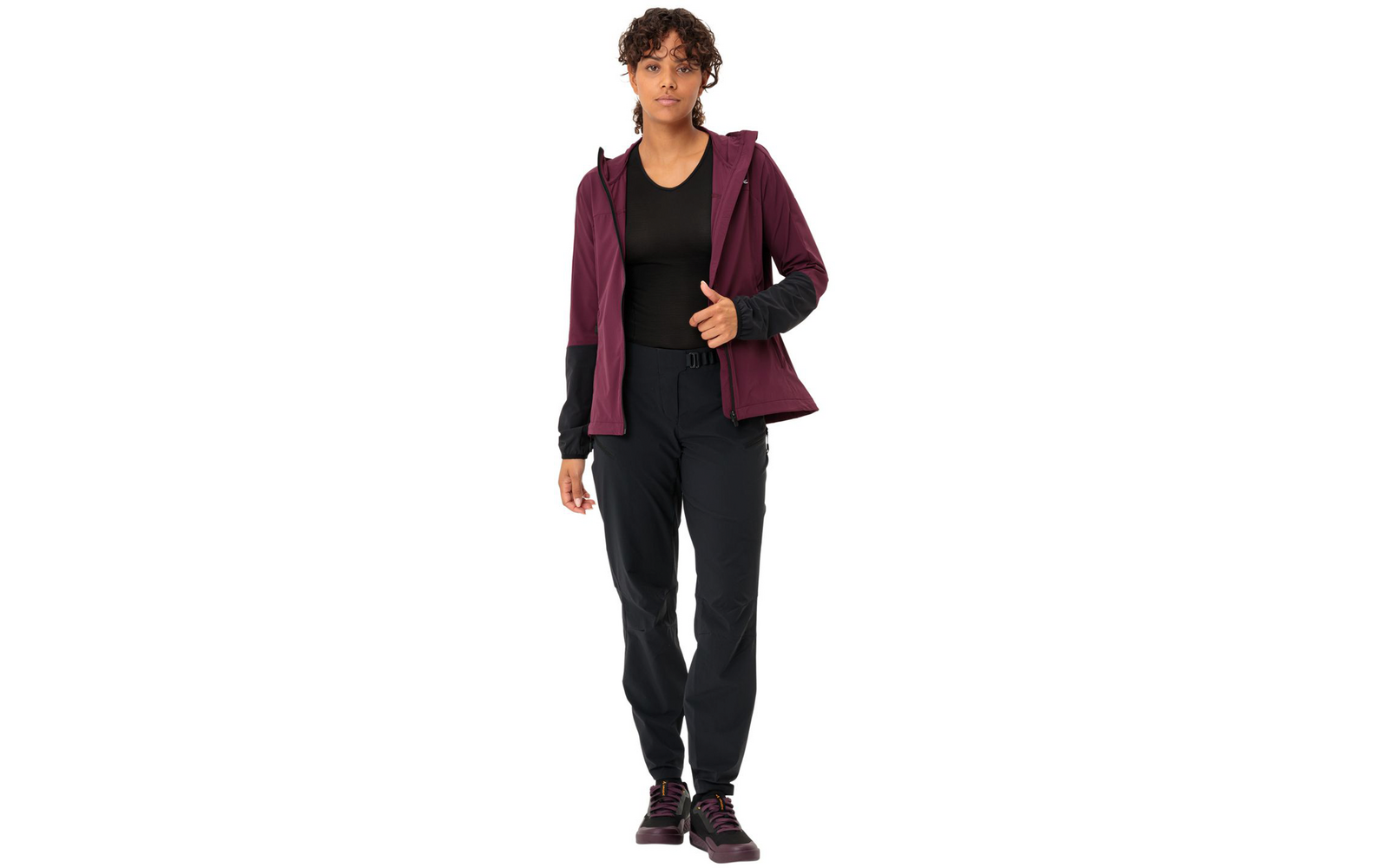 Femme aux cheveux courts et foncés portant un pull rouge foncé, une veste noire, un pantalon noir et des chaussures noires, tenant un sac rouge