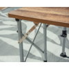 Plateau de table en bois avec pieds métalliques gris et entretoises diagonales sur un tapis gris clair à motifs de feuilles blanches