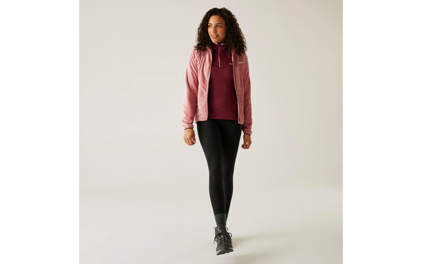 Eine Frau geht, trägt einen rosa Mantel, ein rotes Oberteil und schwarze Hosen