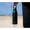 Hand hält schwarze Trinkflasche mit silbernem Verschluss und kleinem Logo, grüne Messpfeile mit Text '28,5 cm' und 'Ø 7 cm 500 ml', Sandstrand, Meer und Himmel im Hintergrund