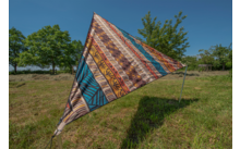 Bunt gemusterte Dreiecksplane auf einer Wiese vor blauem Himmel und Bäumen