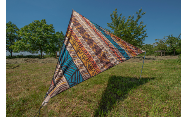 Bunt gemusterte Dreiecksplane auf einer Wiese vor blauem Himmel und Bäumen