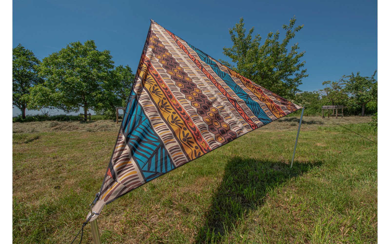 Bunt gemusterte Dreiecksplane auf einer Wiese vor blauem Himmel und Bäumen