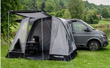 Campingzelt mit Vorzelt neben einem grauen Van auf einer Wiese mit Bäumen im Hintergrund