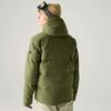 Person von hinten in olivgrüner, gesteppter Jacke mit Kapuze, trägt beige Strickmütze und hochgeschobene Skibrille; hellbeige Hose; heller Hintergrund