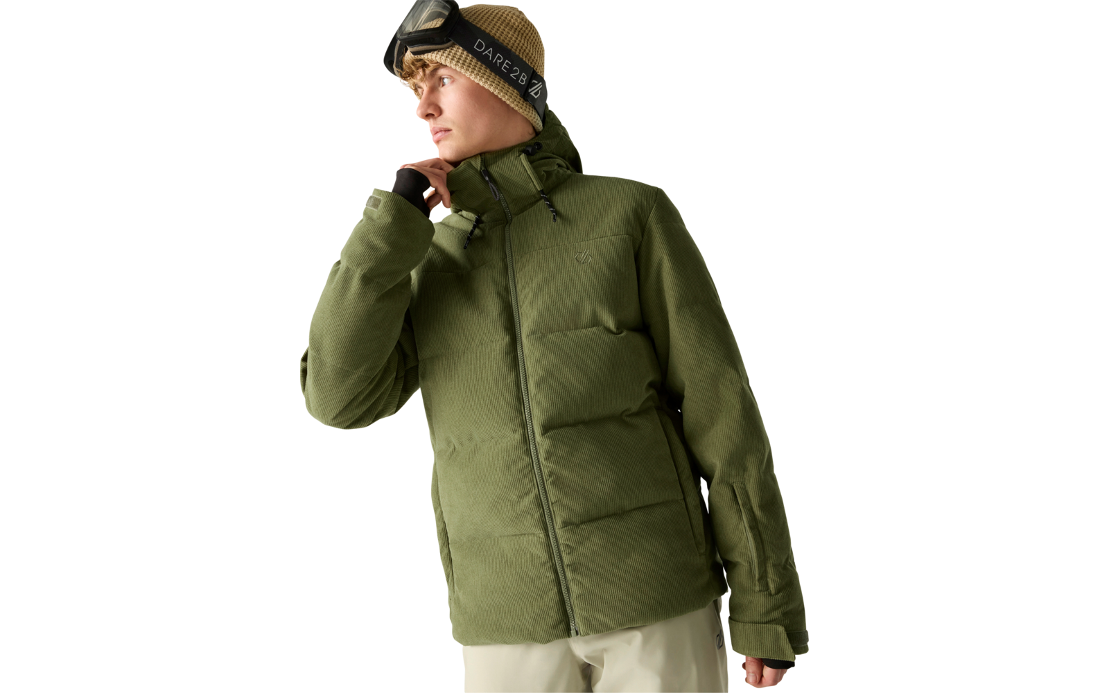 Person in grüner Winterjacke und hellbrauner Mütze mit Skibrille, blickt nach links, helle Hose, neutraler Hintergrund